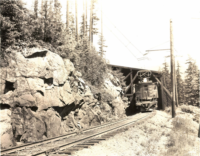 An electric locomotive emerging from a snow shed in the 1900s.